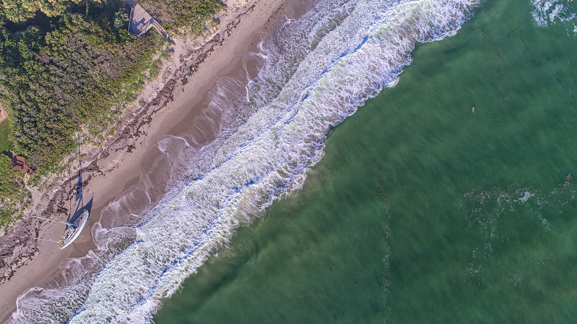 An aerial view of Melbourne Beach, Florida, showing the narrow barrier island with the Atlantic Ocean on one side and the Indian River Lagoon on the other.